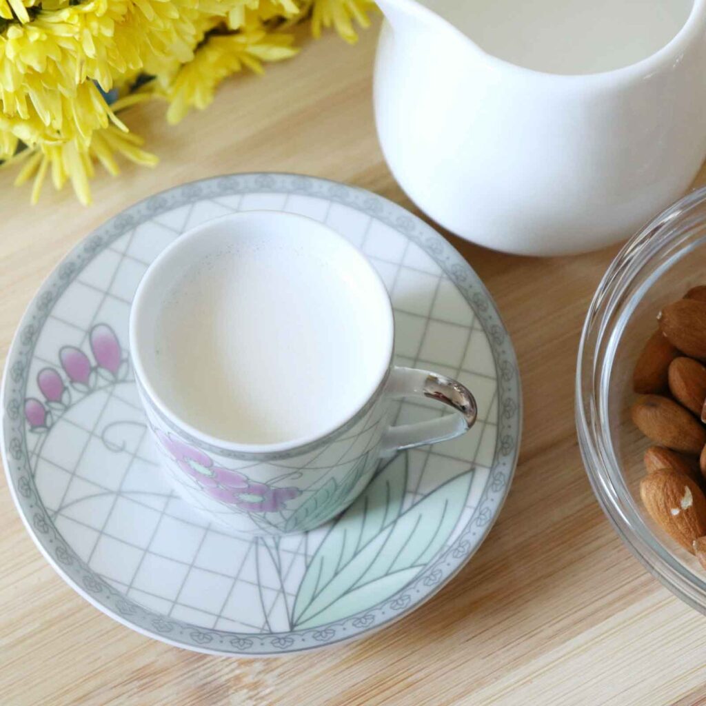 Freshly made milk at home. A cup of dairy-free milk with nuts and yellow flowers on a wooden table.