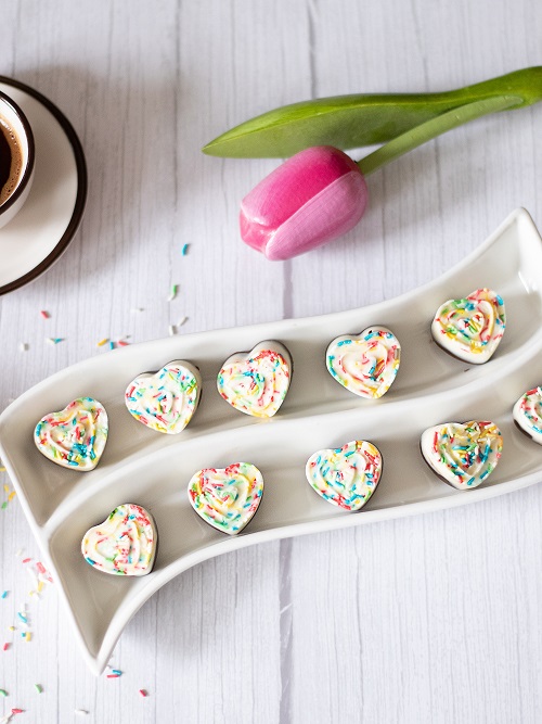 Dark and white chocolate hearts with rainbow sprinkles on a wooden table with coffee and tulip. Easy dessert recipe for homemade chocolate hearts.