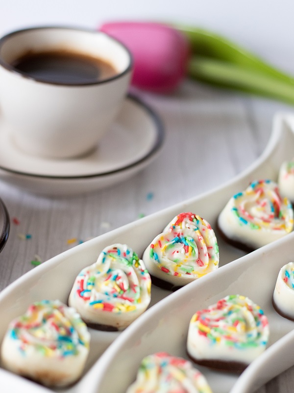 Sweet and cute chocolate rainbow hearts on white plate with coffee and flower in the background. Quick, vegan dessert idea.