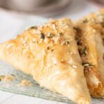 This blog post is about how to make baklava at home. Close up of piece of baklava garnished with chopped pumpkin seeds and nuts.