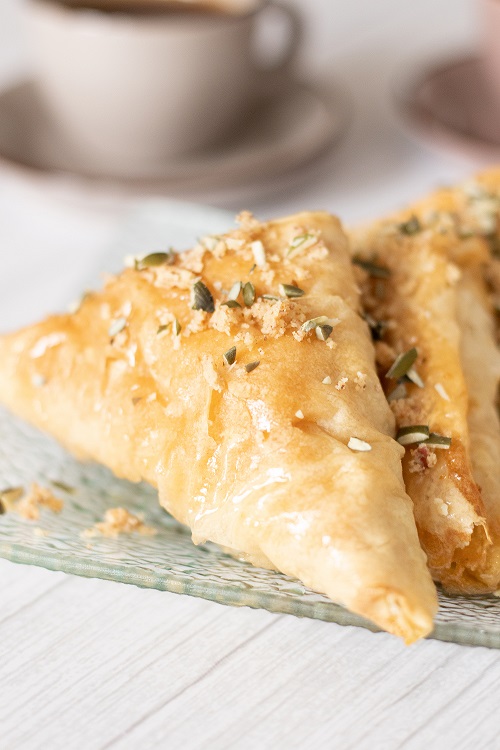 This blog post is about how to make baklava at home. Close up of piece of baklava garnished with chopped pumpkin seeds and nuts.