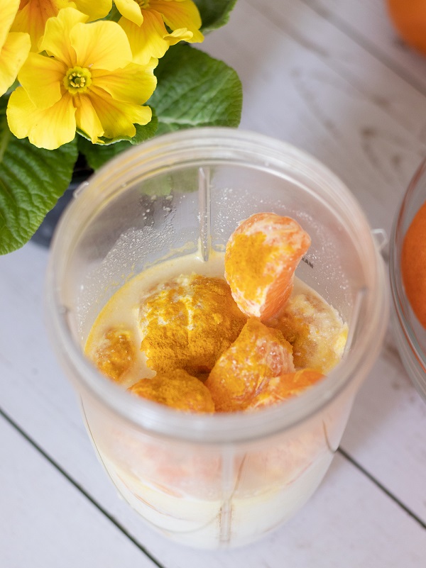 Healthy ingredients for vegan smoothie: oranges, tangerines, bananas, cashew milk, and turmeric powder.
