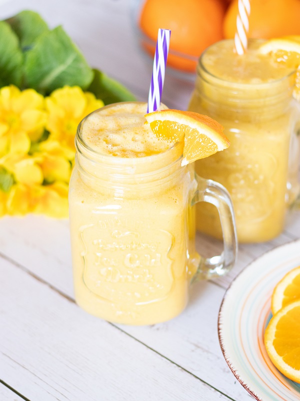 Immune booster orange smoothie jar on wooden background with flowers and fresh oranges. Quick and easy recipe for breakfast.