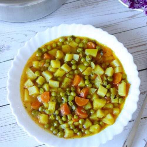 In this post I describe how to make homemade green peas recipe for lunch. A full plate of green peas stew with vegetables on wooden table served with salad as side dish.