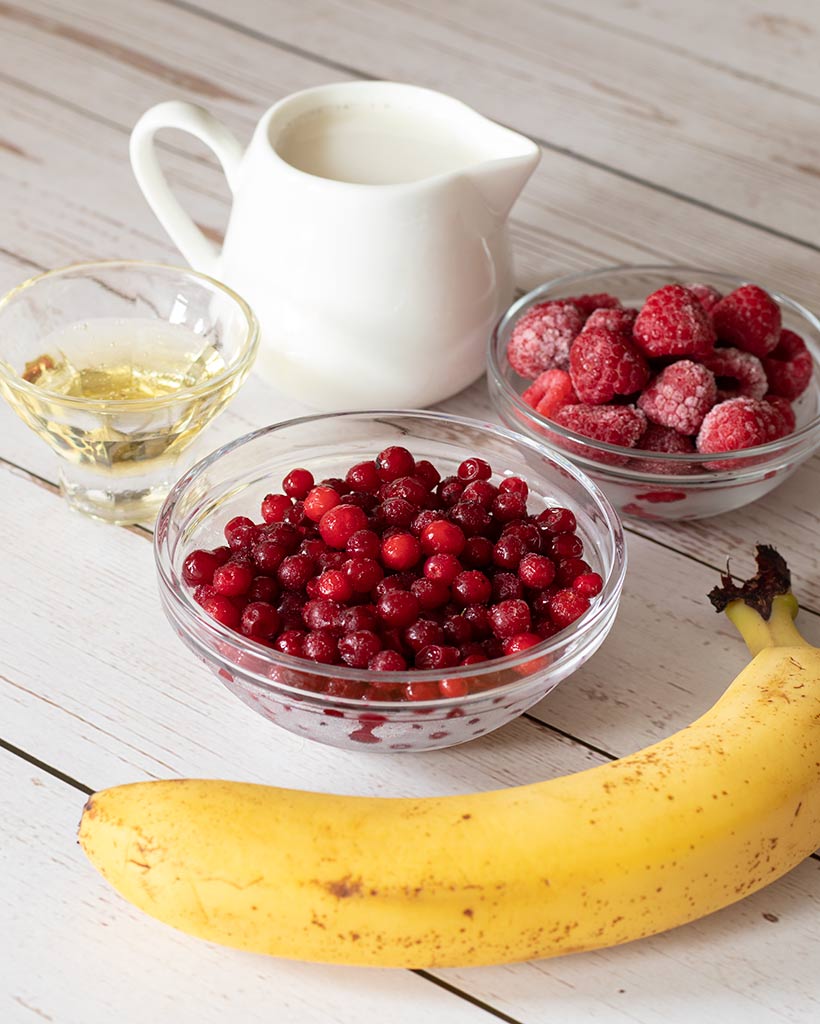 Simple wholesome plant-based healthy ingredients for morning breakfast smoothie recipe: frozen cranberries, raspberries, banana, agave and almond milk.
