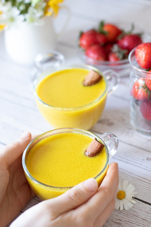 Sweet and creamy turmeric golden milk with cinnamon sticks on wooden table with fresh strawberries and flowers