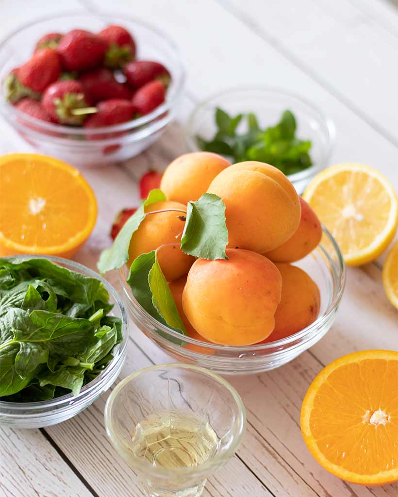 Wholesome, plant-based, natural ingredients for preparing raw salad with apricots, strawberries and spinach.