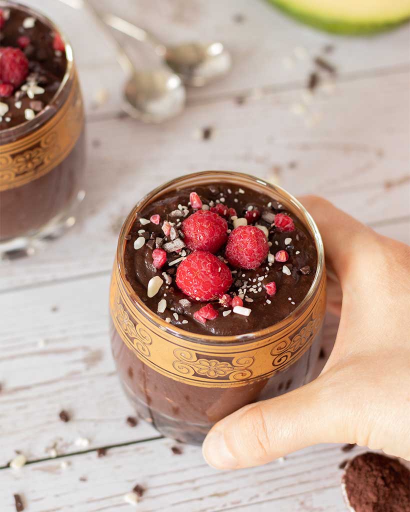 A hand holding a glass of naturally sweetened avocado mousse on wooden table. Tasty, kid-friendly snack or dessert idea.