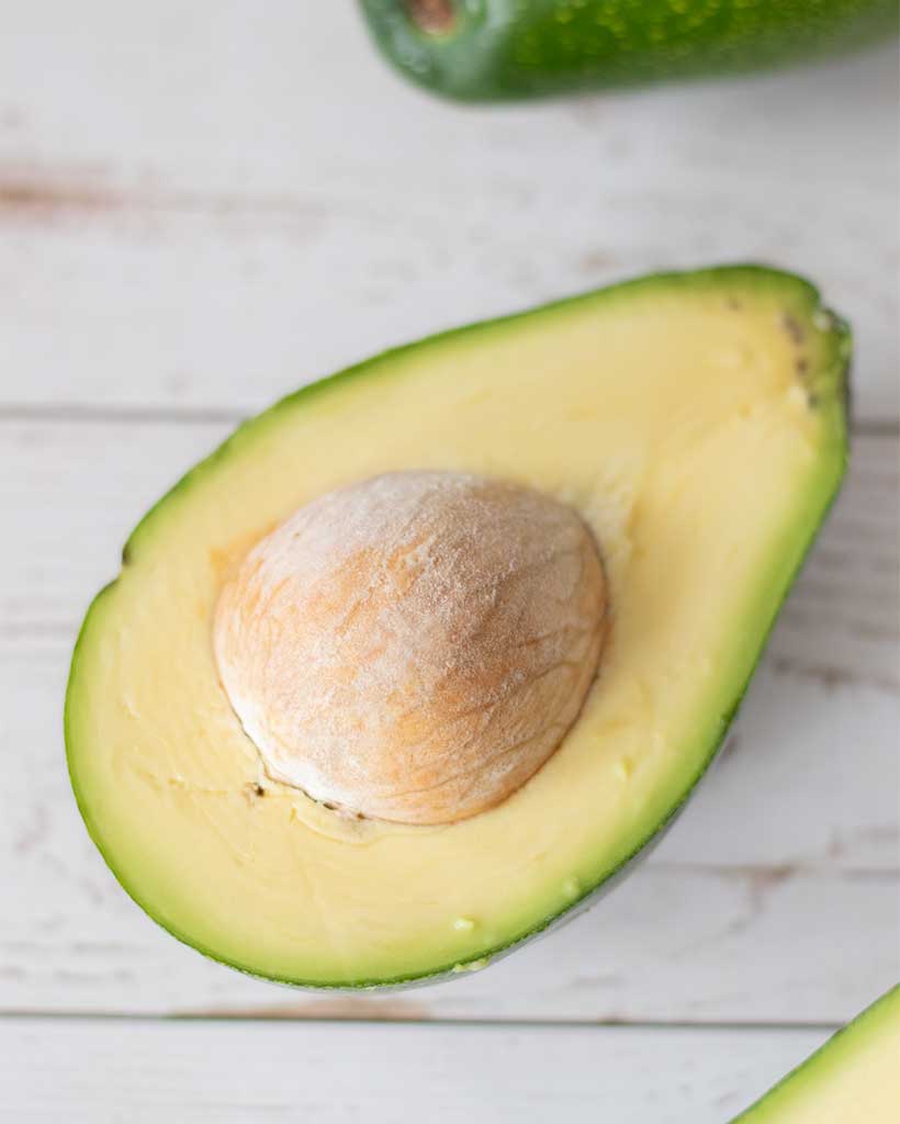 Fresh and ripe avocado sliced in half on wooden table.