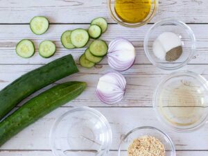 Wholesome and fresh ingredients for making plant-based salad with cucumbers, red onion, sesame seeds and simple apple cider vinegar and olive oil vinaigrette. Weight loss friendly side dish.
