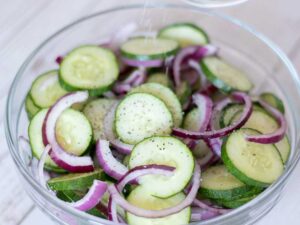 Thinly sliced cucumbers and red onion for salad in a bowl.