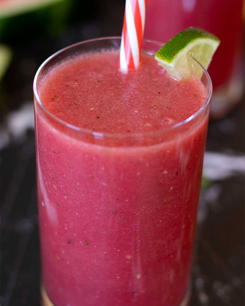 Tasty watermelon smoothie without yogurt in a big glass with straw decorated with fresh lime.