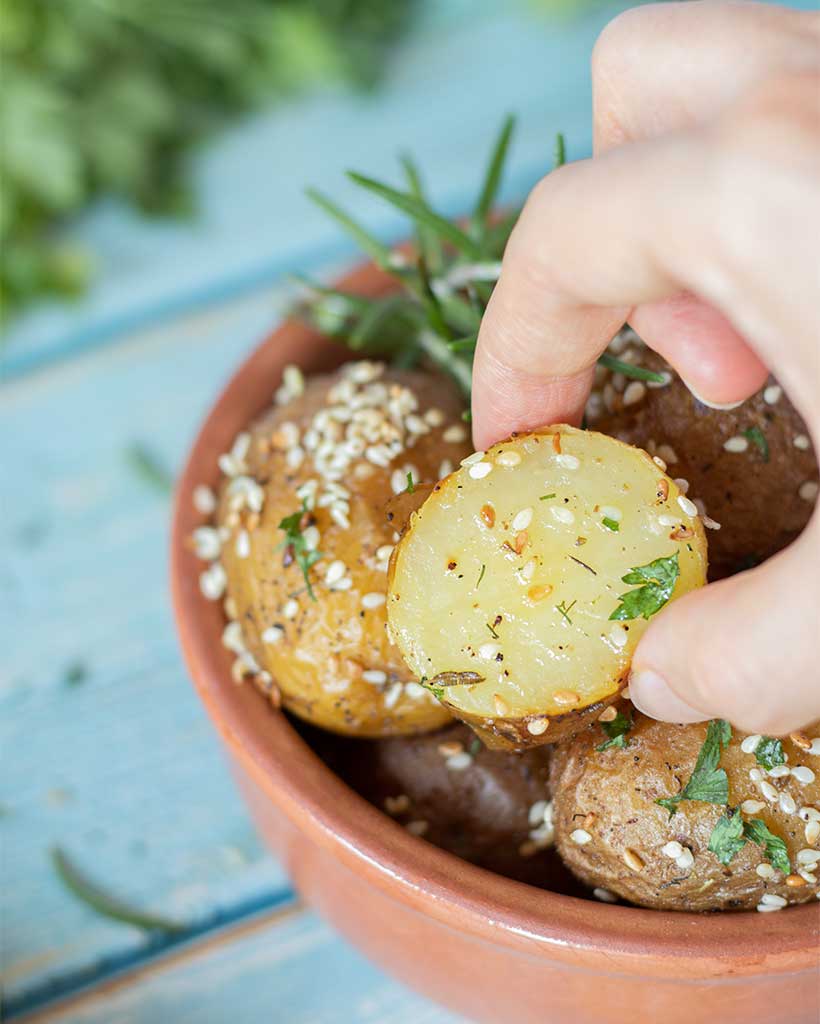 Perfectly whole roasted baby potatoes in the oven for side dish, lunch, dinner, or appetizer. Mini potato cut in half and woman's fingers taking hold of it.