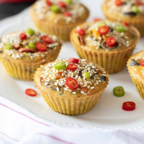 Mini chickpea flour frittatas, vegan-friendly savoury breakfast or snack decorated with sesame seeds and finely chopped red and green peppers on white plate.