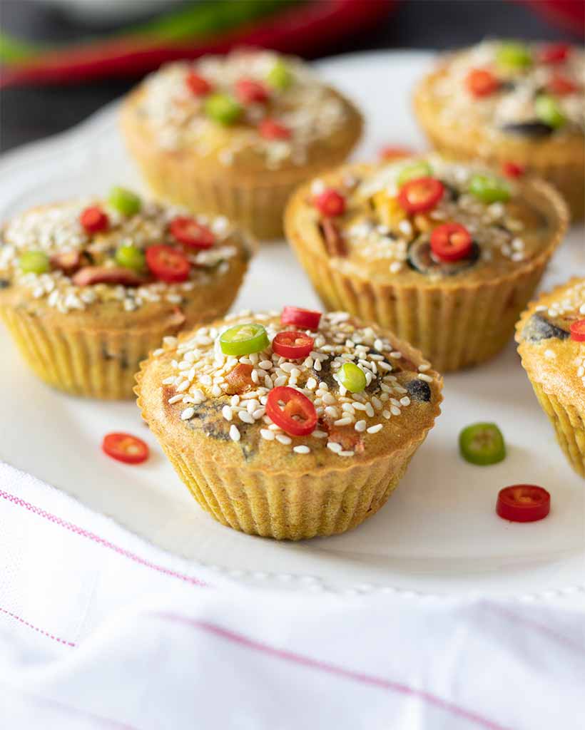 Mini chickpea flour frittatas, vegan-friendly savoury breakfast or snack decorated with sesame seeds and finely chopped red and green peppers on white plate.