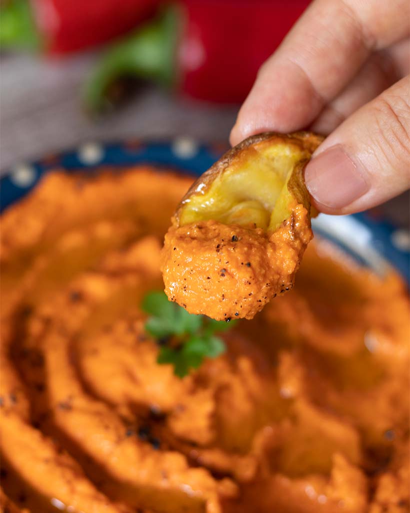 Potato chips dipped in delicious and creamy homemade hummus dip with vibrant orange-red color for healthy snack.