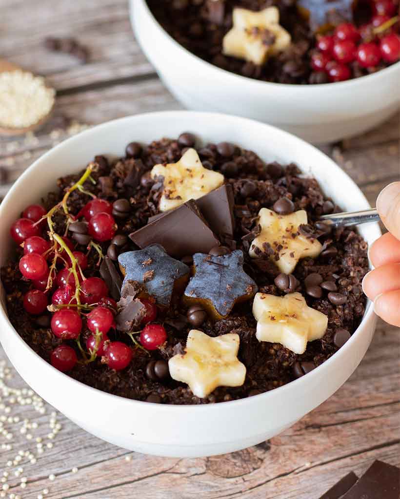 High-protein, dairy-free and gluten-free chocolate quinoa breakfast bowls decorated with dark chocolate and fresh fruits on wooden table.