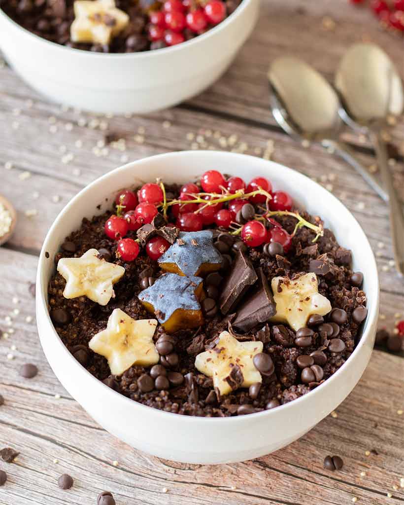 A chocolate bowl full of cooked superfood quinoa and fresh fruits. Dairy-free meal prep recipe idea.