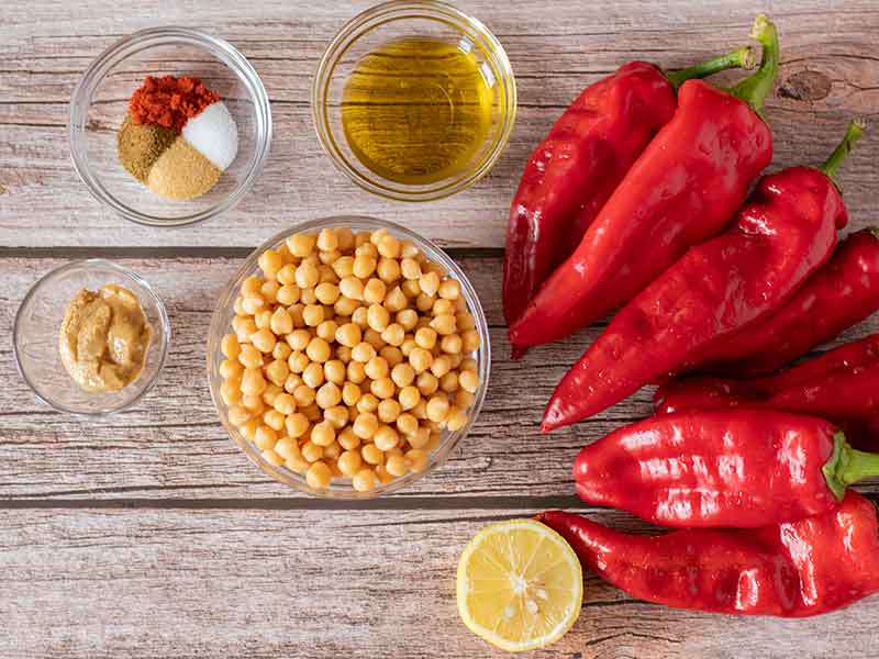 Wholesome, plant-based, clean eating ingredients for preparing homemade vegetarian hummus: roasted red peppers, chickpeas (garbanzo beans), olive oil, lemon juice, tahini and spices.