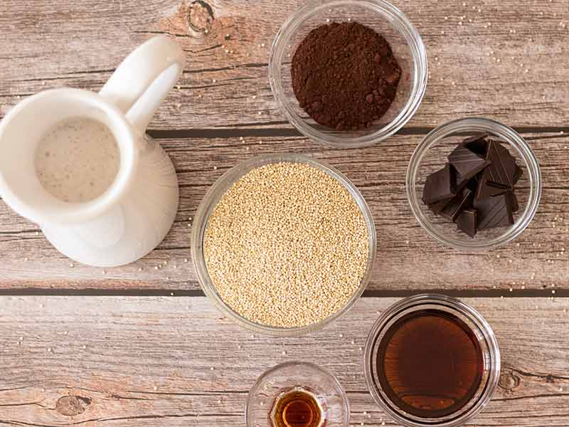 Wholesome, plant-based ingredients for preparing delicious, sweet gluten-free dish: white quinoa, maple syrup, almond milk, dark chocolate, cacao powder and pure vanilla extract.