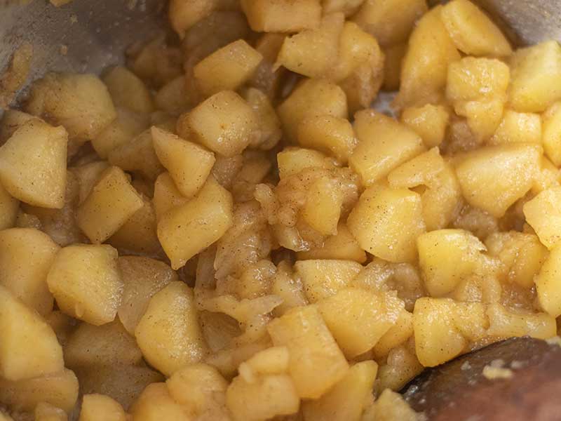 Chopped apples, ground cinnamon, lemon juice, and water in a cooking pot on the stovetop.