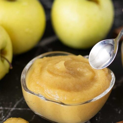 Delicious kid-friendly sweet applesauce without sugar in a with Golden Delicious Apples in the background.