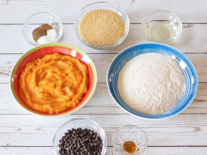 Simple, low cost, budget-friendly  ingredients for baking homemade and wholesome pumpkin cookies: pumpkin puree, spelt flour, unrefined brown sugar, vegan chocolate chips, sunflower oil, vanilla extract and spices.