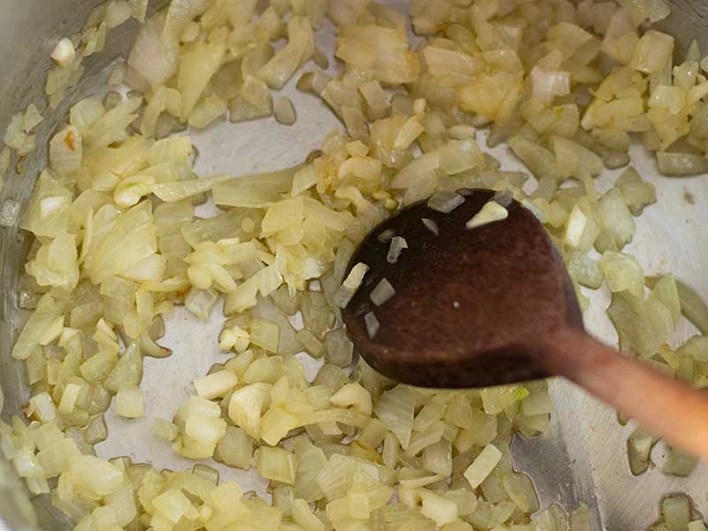 Finely chopped onion and garlic cooking on the stovetop in big pot for preparing low fat, low-calorie vegetarian stew.