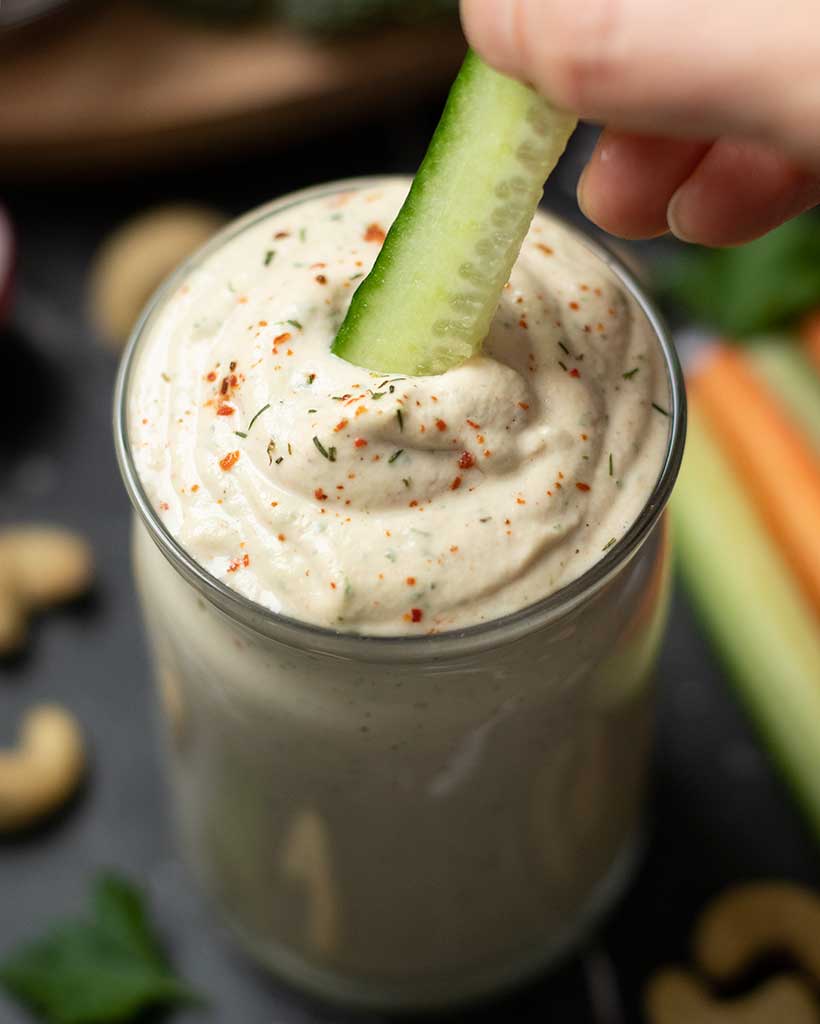 A piece of cucumber dipped in plant-based, dairy-free ranch as an appetizer or snack.