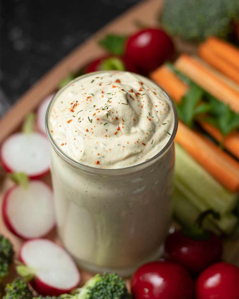 Vegan ranch dressing recipe (no mayo, oil-free). Creamy dairy-free dip in a small jar with fresh chopped vegetables.