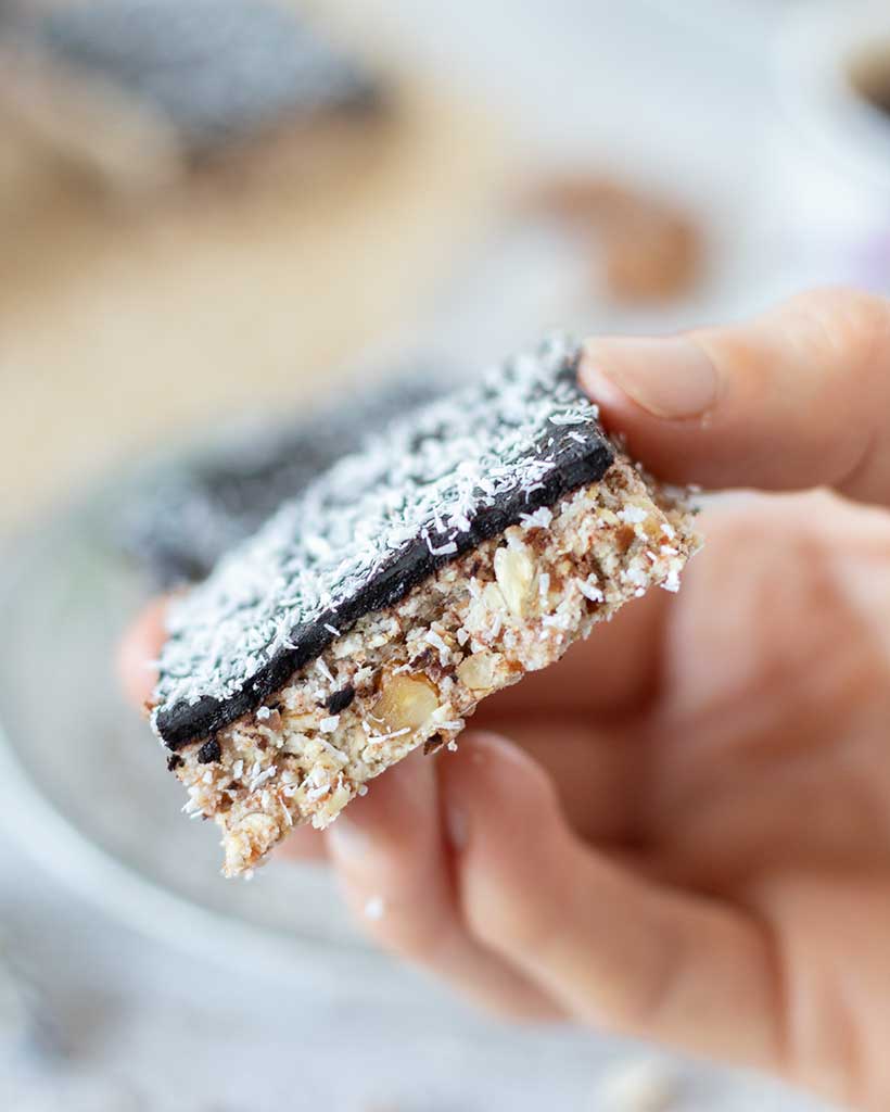 A piece of almond milk pulp cake topped with homemade dark chocolate and coconut flakes.