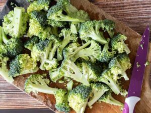 Chopped broccoli florets on wooden cutting board with purple knife