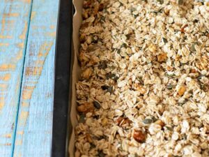 Homemade granola mixture arranged in one layer in a baking sheet.
