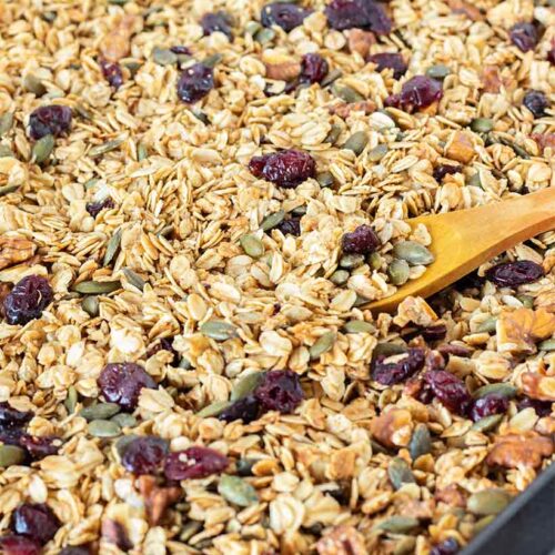 Homemade granola recipe healthy breakfast, snack, brunch or dessert idea. Gluten free freshly baked granola on a baking tray lined with parchment paper and a wooden spoon.