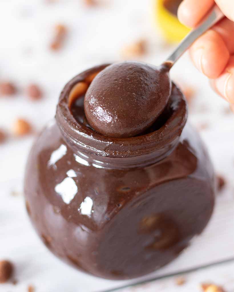 A spoonful of homemade Nutella with a jar full of tasty vegan hazelnut butter.
