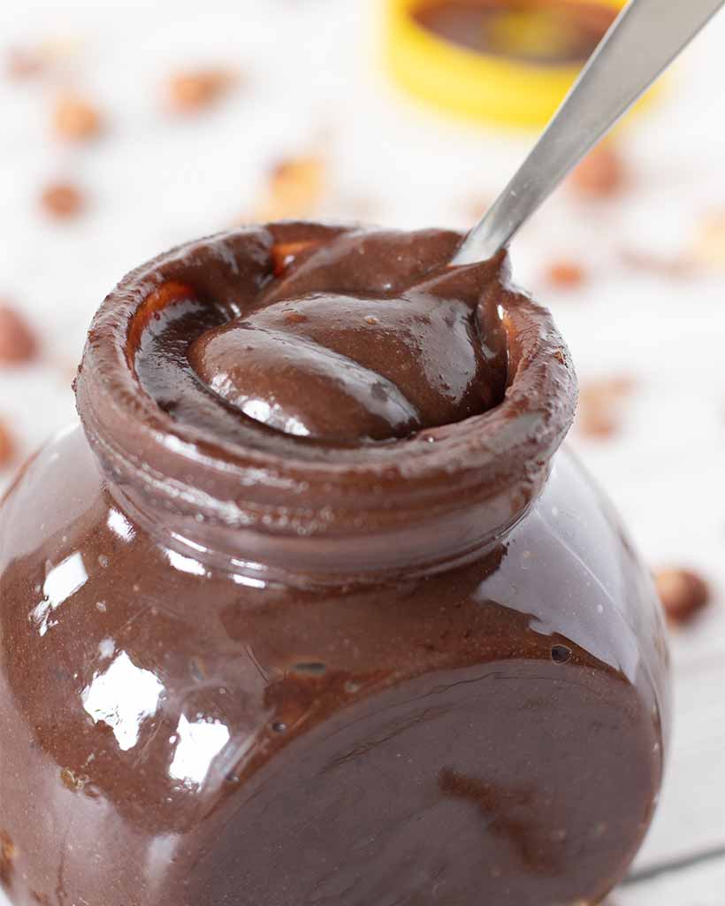 Recipe for homemade Nutella. Best vegan hazelnut spread in a glass jar with spoon.