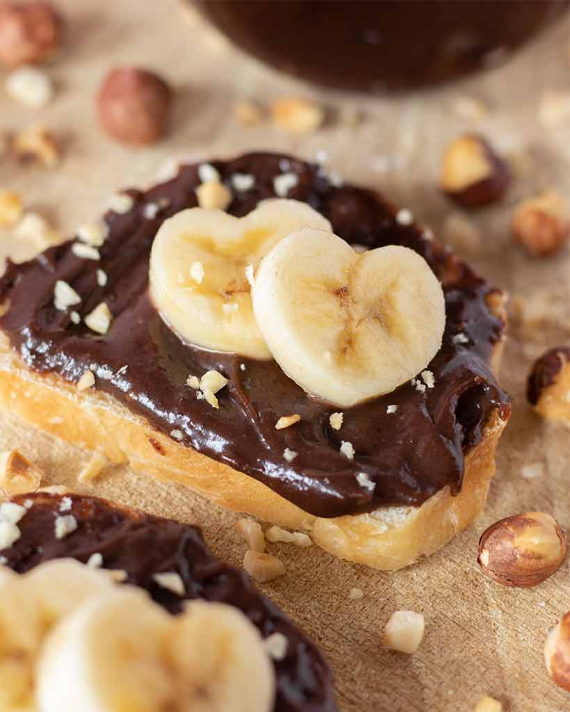 Smooth and creamy chocolate hazelnut spread on crusty slices of bread decorated with banana hearts with roasted hazelnuts.