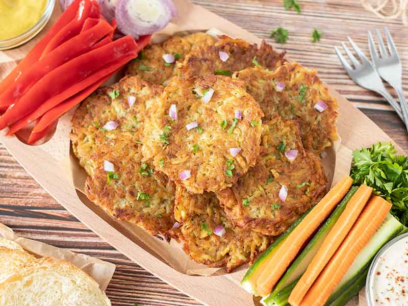 Yummy, crispy vegan latkes in a big wooden plate served with fresh vegetables for lunch or dinner.