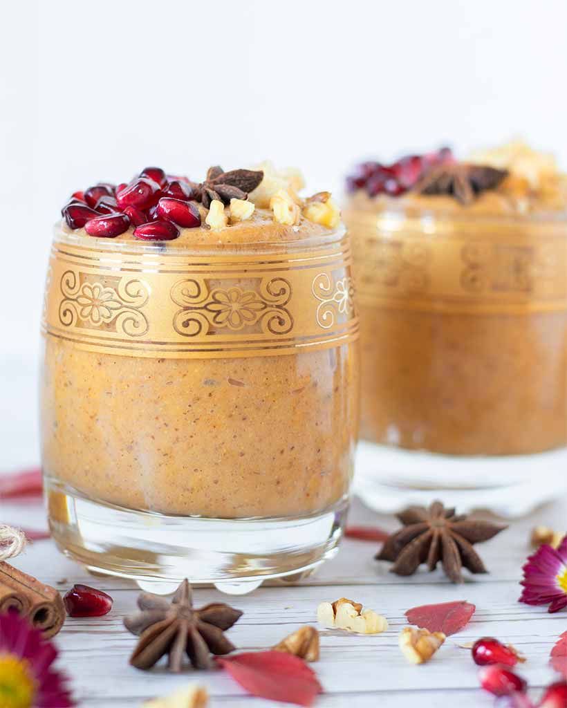 No yogurt, no sugar creamy pumpkin smoothie that tastes like an autumn dessert divided in two glasses on wooden table with red leaves, cinnamon, flowers and walnuts.