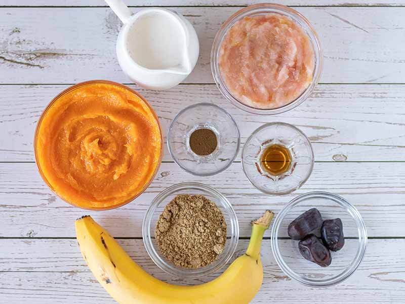 Simple, plant-based, clean ingredients for making delicious and creamy homemade pumpkin smoothie: pumpkin puree, applesauce, almond milk, dates, banana, vanilla extract, flaxseed meal and ground cinnamon.