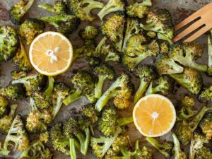 Warm oven roasted broccoli layered on a baking sheet lined with parchment paper with fresh lemon and seasonings.