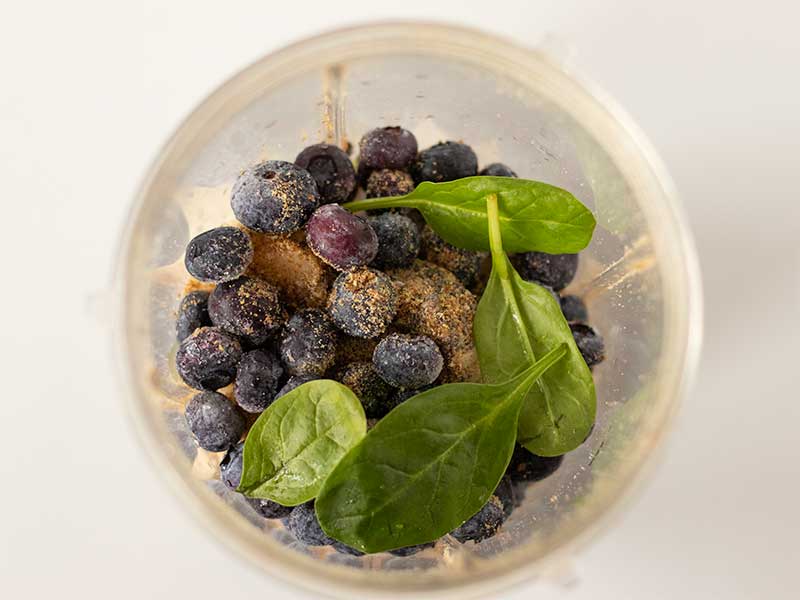 Plant-based wholesome ingredients for making homemade blueberry smoothie recipe to lose weight: frozen blueberries and banana, fresh spinach, oat milk, ground flaxseed and chia seeds.