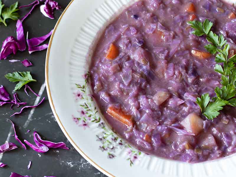 Colorful purple vegetables soup in a plate garnished with fresh parsley leaves on a table with finely chopped cabbage.