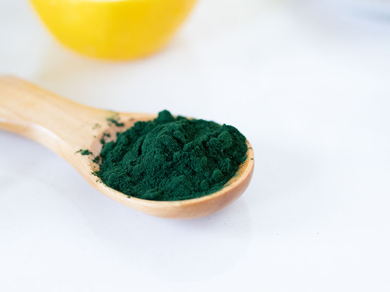 Green spirulina powder in a wooden spoon.