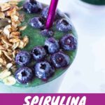 Healthy green high-protein spirulina smoothie in a glass topped with granola and blueberries.