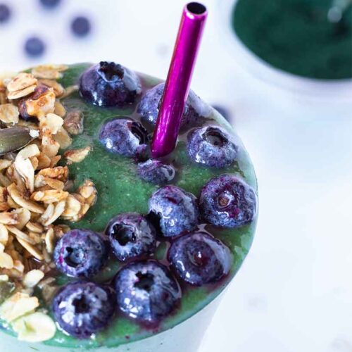 Green spirulina smoothie for weight loss and fat burning. Healthy and tasty morning breakfast drink. High-protein mix topped with frozen blueberries and homemade granola.