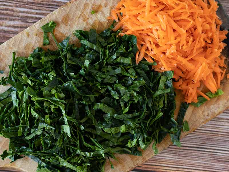 Finely chopped fresh spinach and grated carrots on wooden cutting board for baking savory vegetarian muffins recipe.