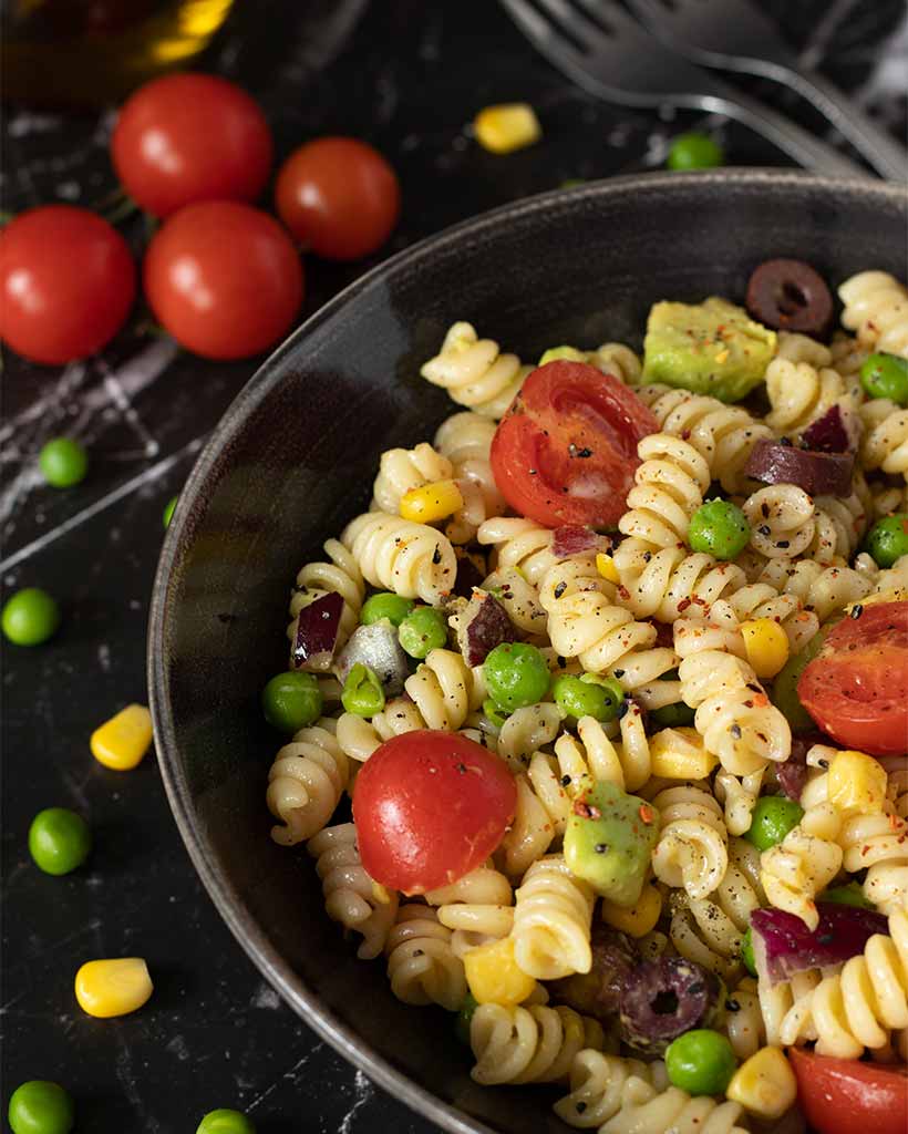 Best cold pasta salad in a dish on black granite table with healthy veggies.