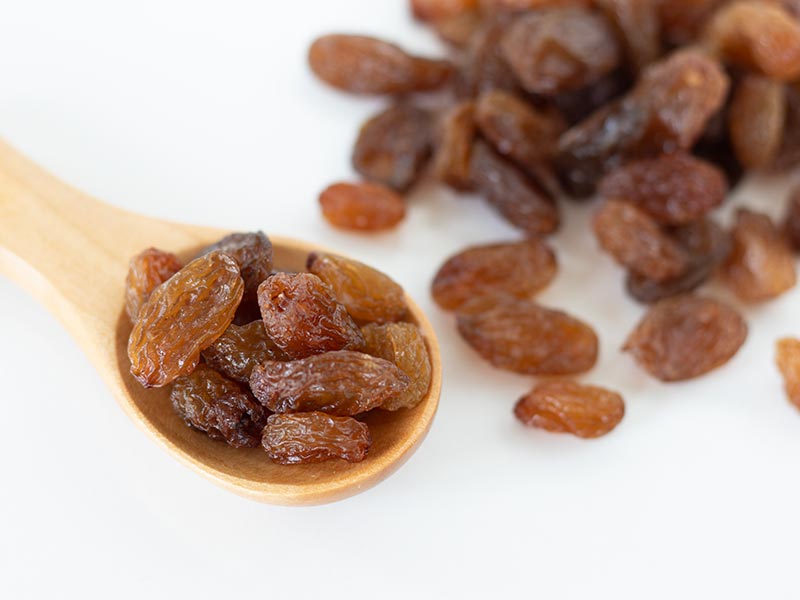 Raisins (dried grapes) in a wooden spoon on white table