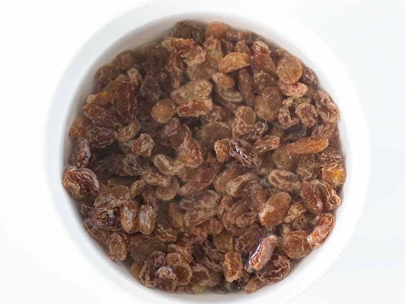 Raisins covered with a hot water to be soaked for baking healthy cookies without sugar.